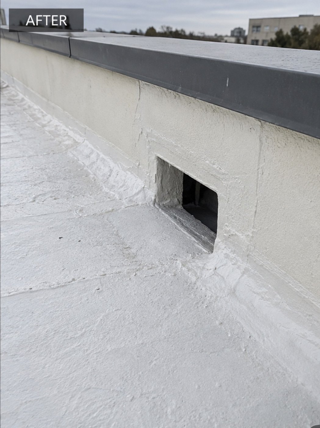 The same scupper after repair, the opening re-detailed and the deck and parapet coated uniformly white